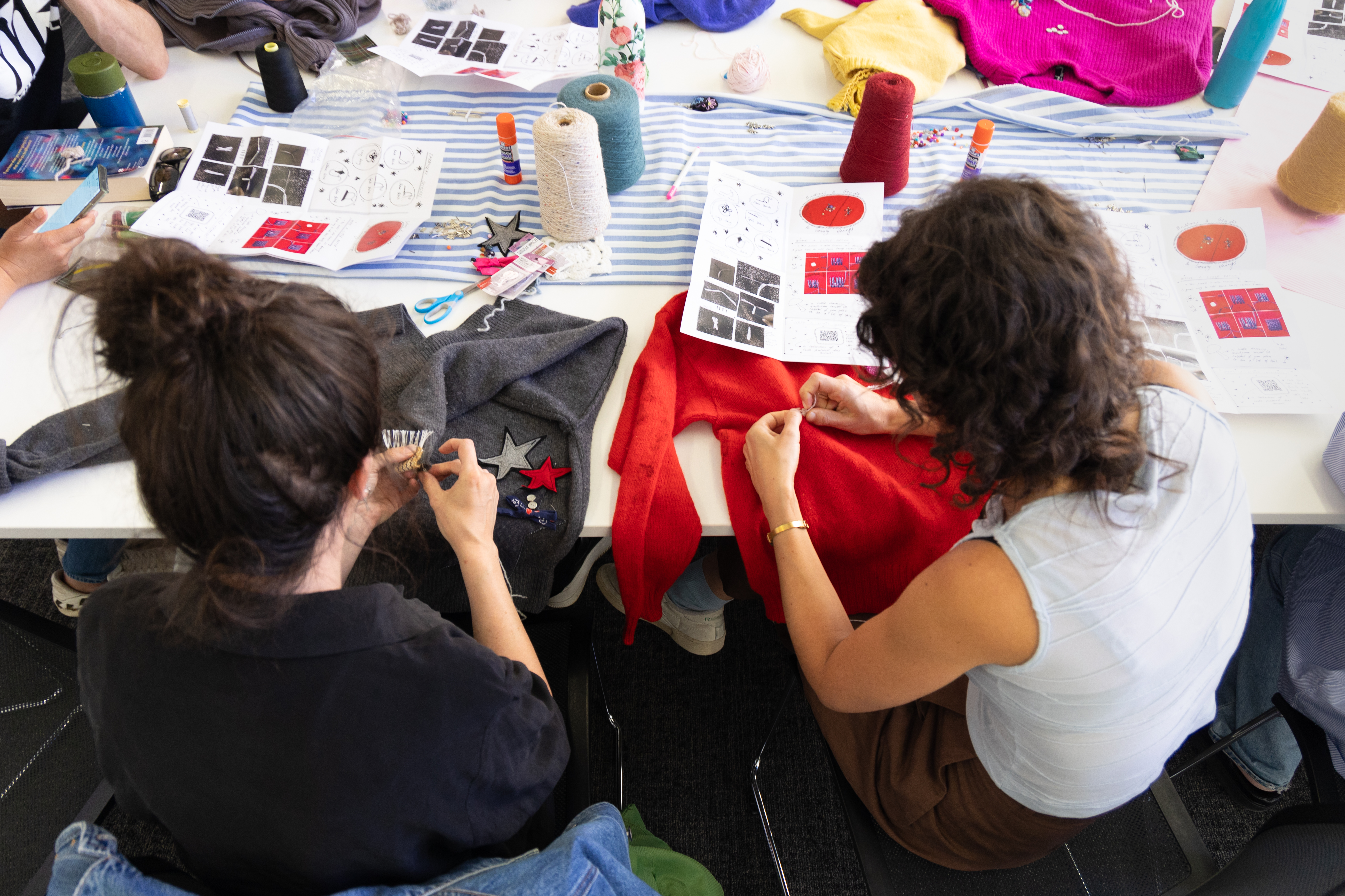 Two Collarts fashion students repairing jumpers by hand sewing on stars