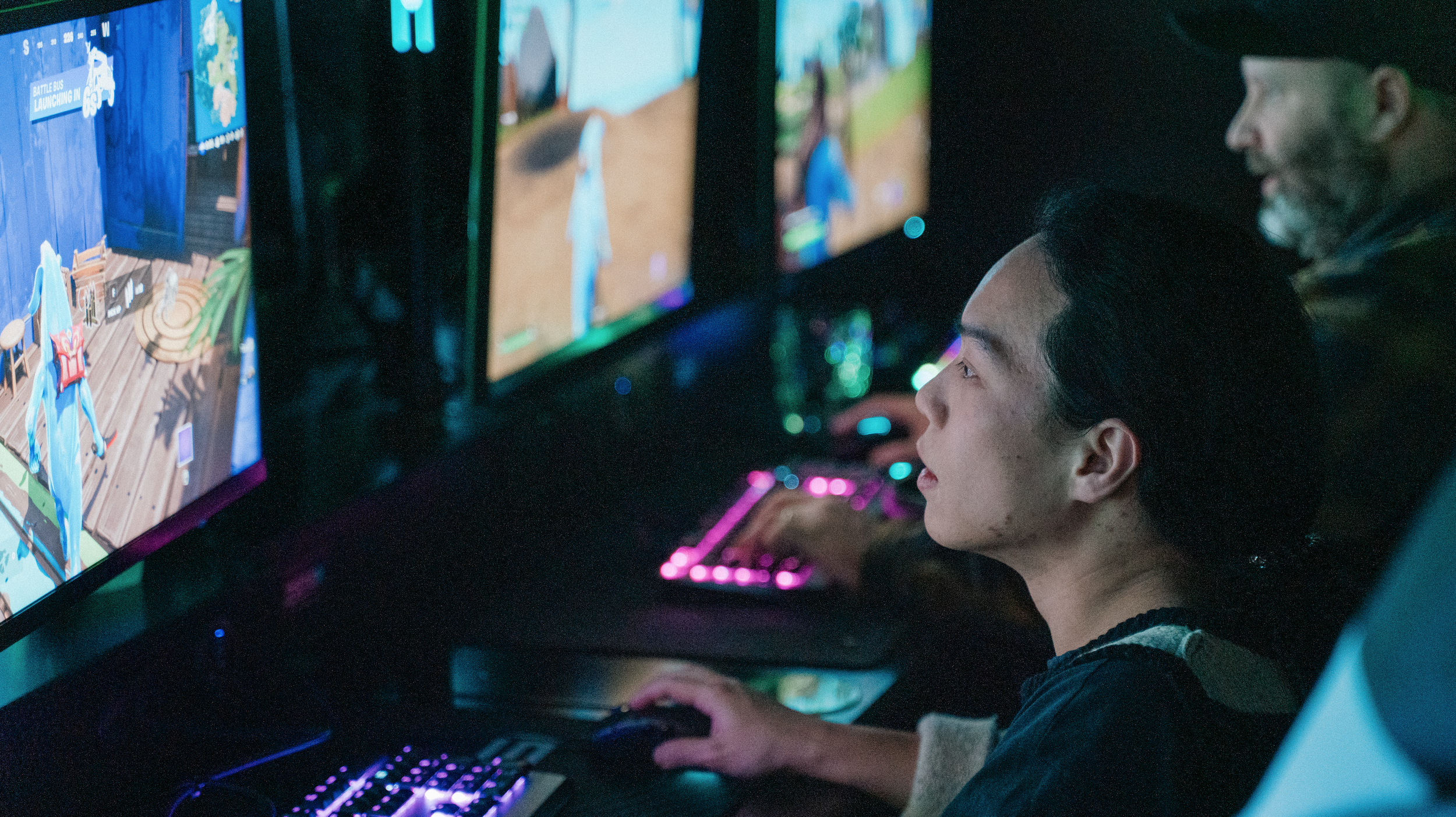Collarts student looking at a screen monitor, playing a video game with their hand on a mouse next to a lit up keyboard.
