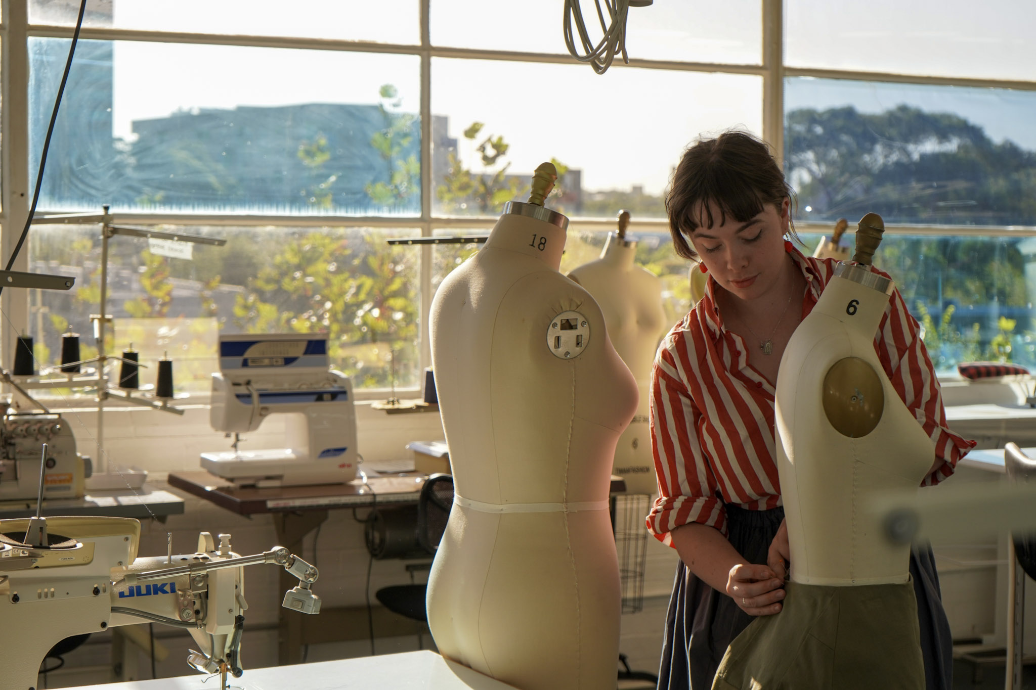 Collarts fashion teacher pinning a skirt on a mannequin in a sunlit classroom